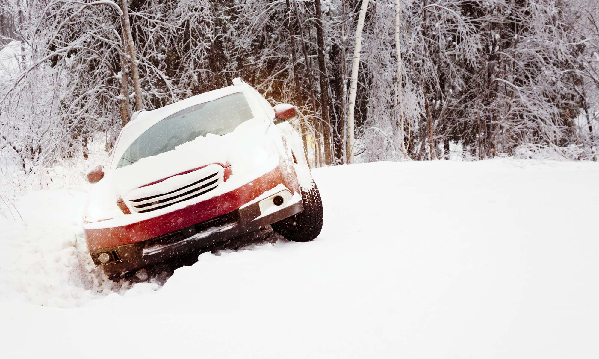 A red car is stuck in a snowbank on the side of the road.