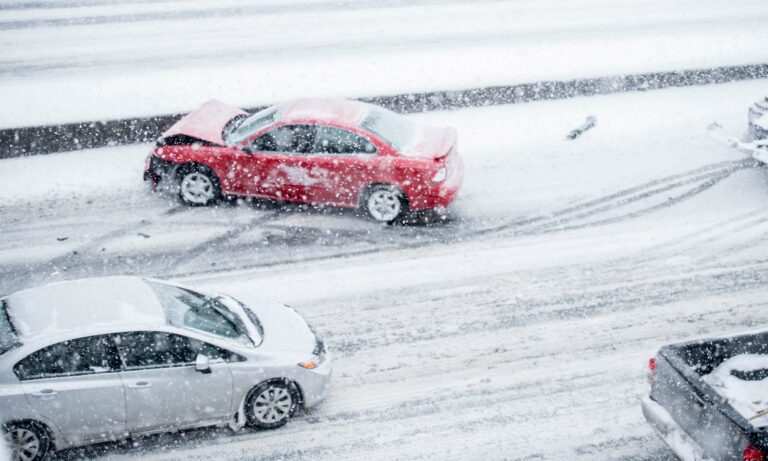 A red compact car sits on the side of a highway after getting in a single-car accident in the snow.