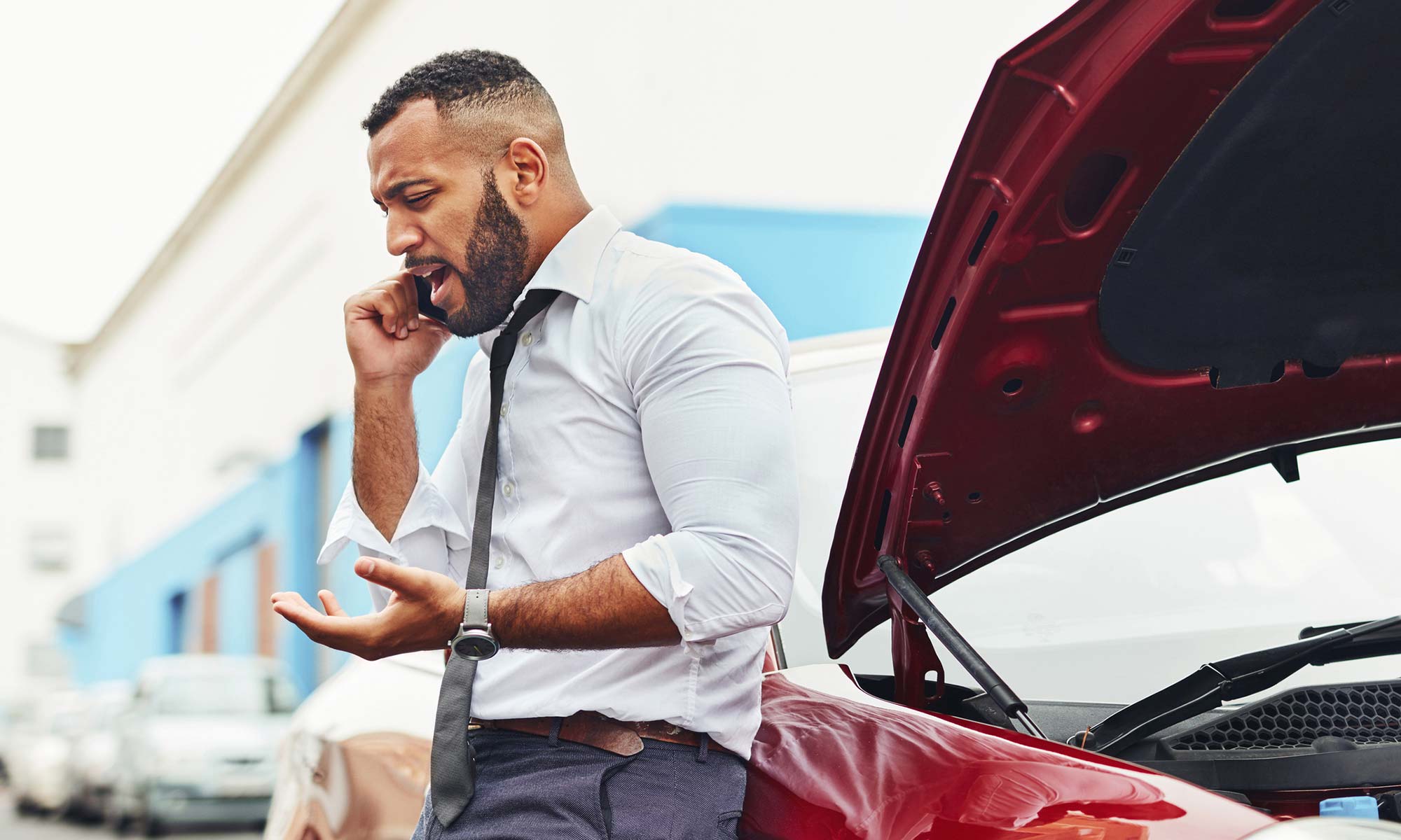 A man talks on the phone next to his broken down vehicle.