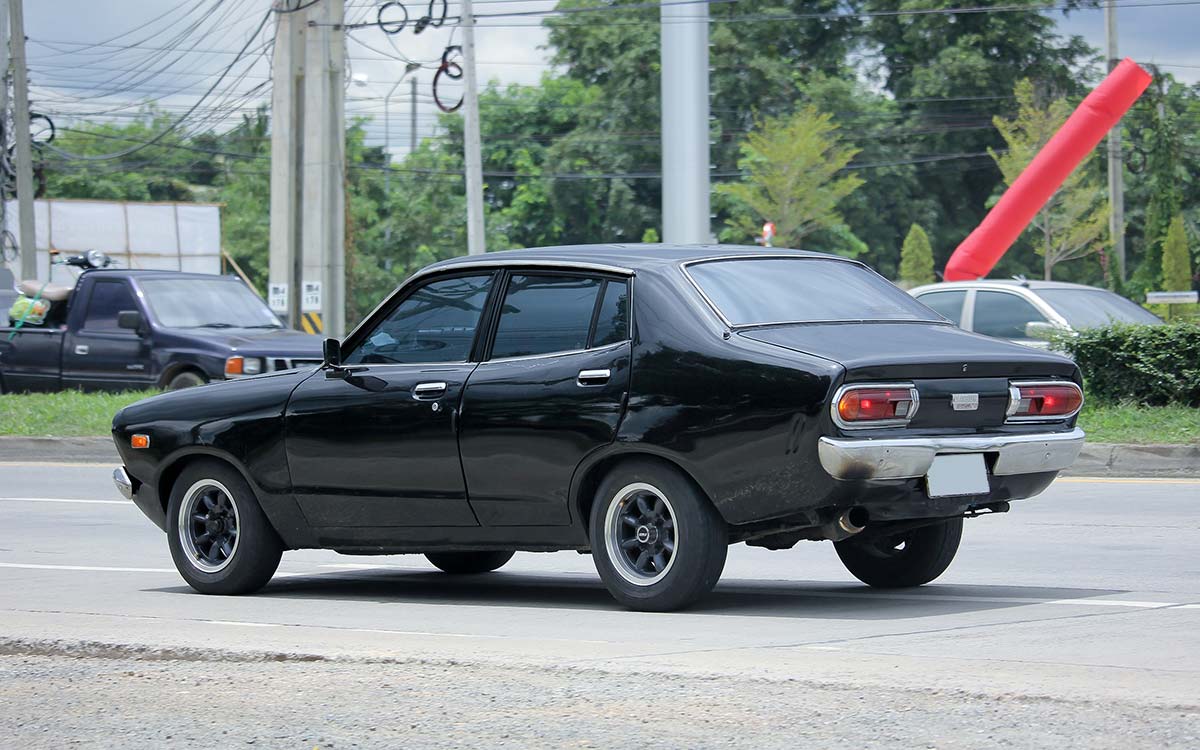 A vintage Datsun 120Y driving down a road.