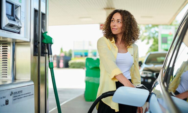 A young woman filling up her car's gas tank at a gas pump.