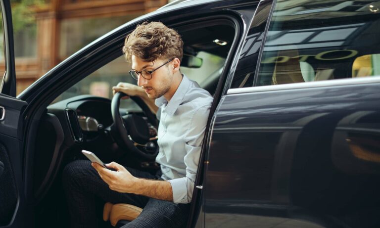 A young man looking for an extended warranty on his phone while sitting in his car.