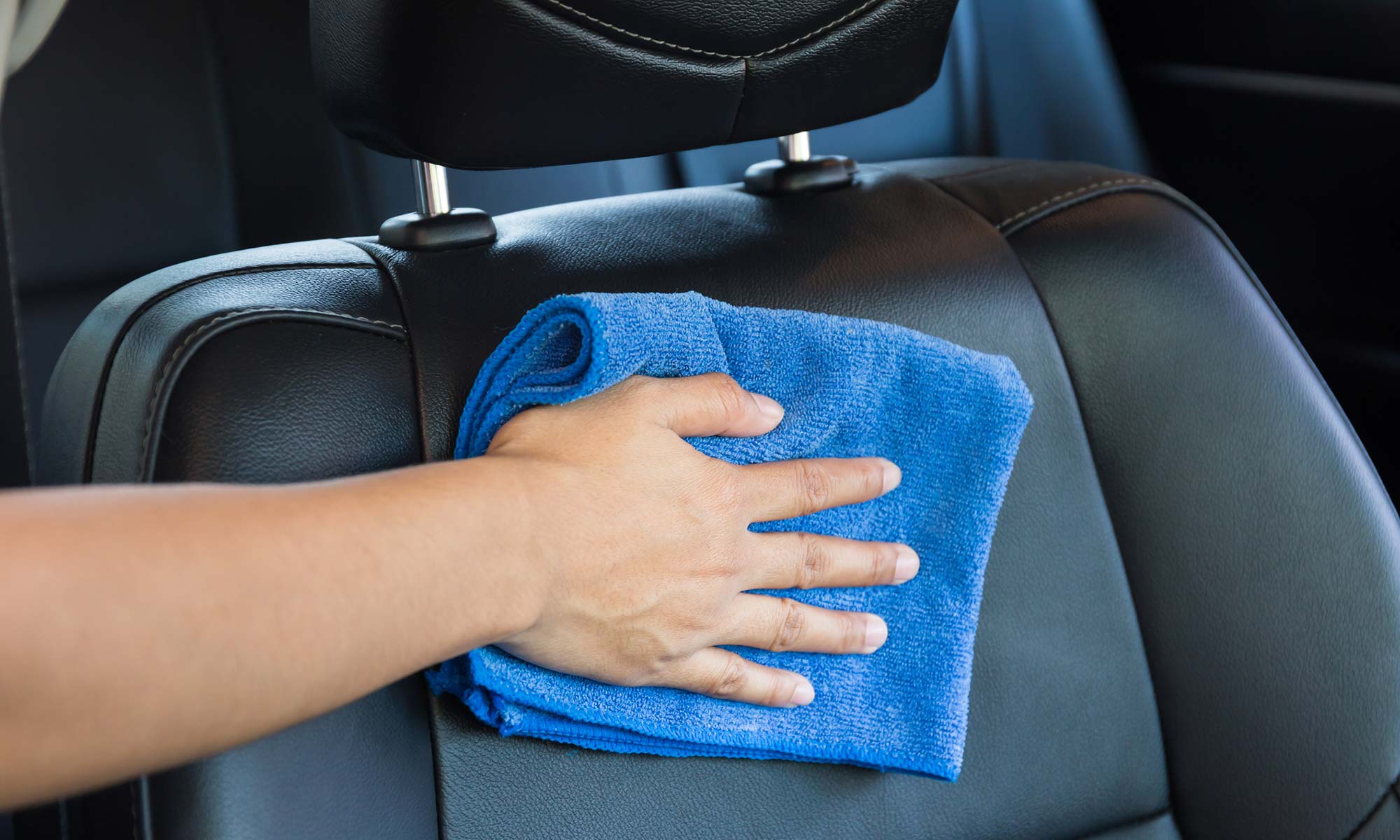 A person wiping a leather car seat with a clean towel.