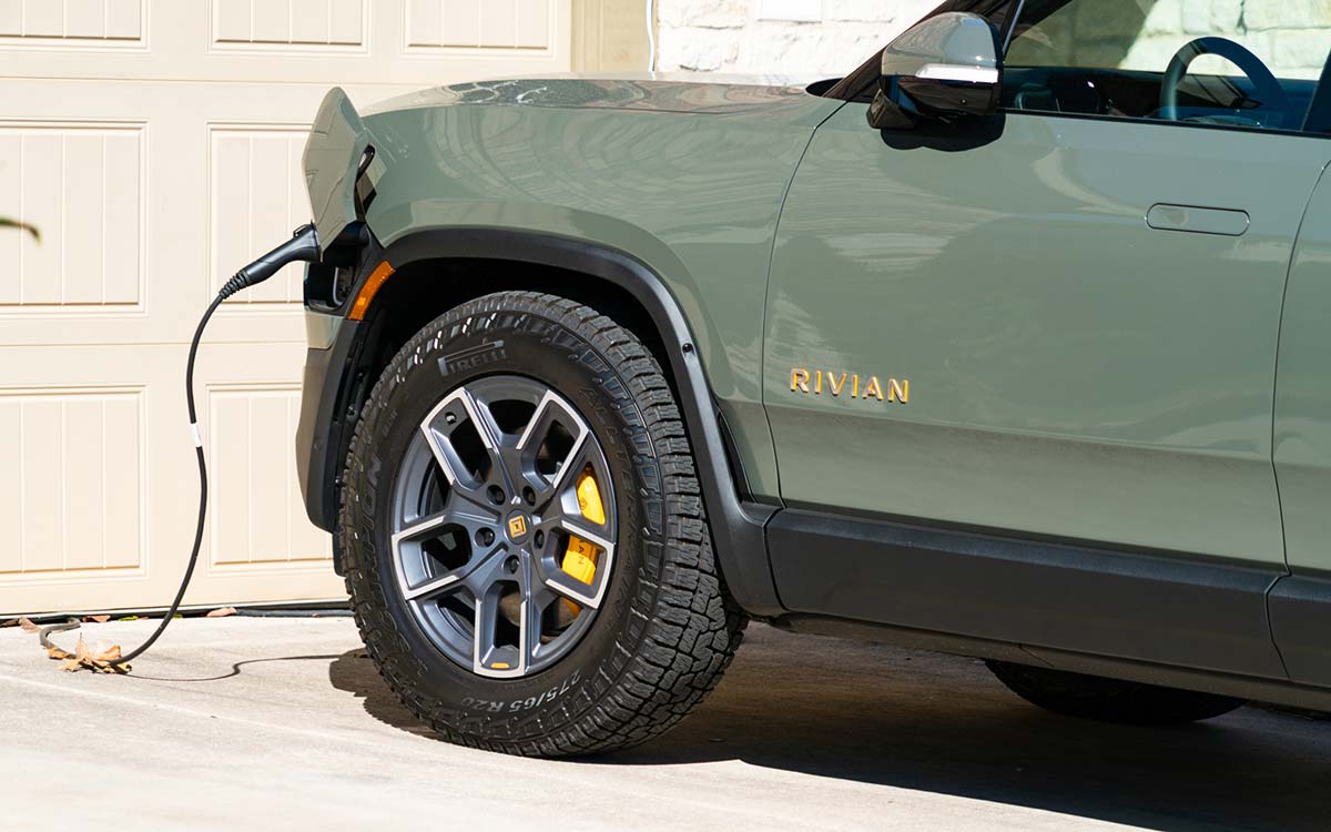 A Rivian R1T truck charges in the driveway of a home.