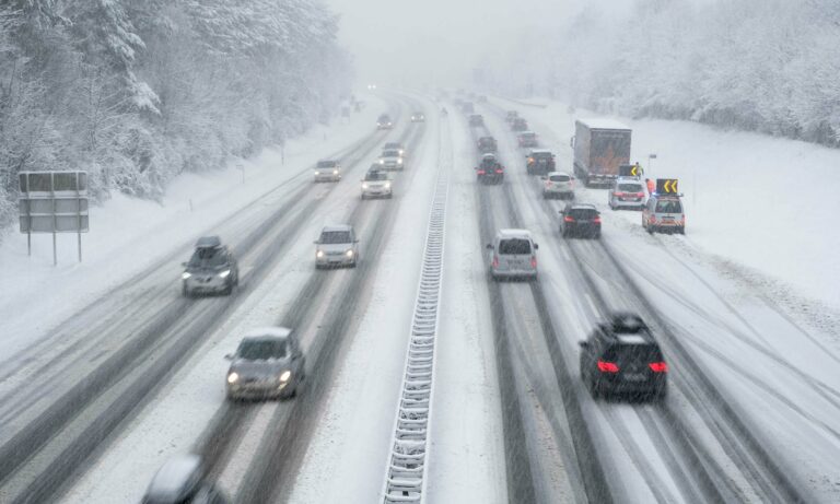 Cars driving on a snow covered highway during a winter storm.