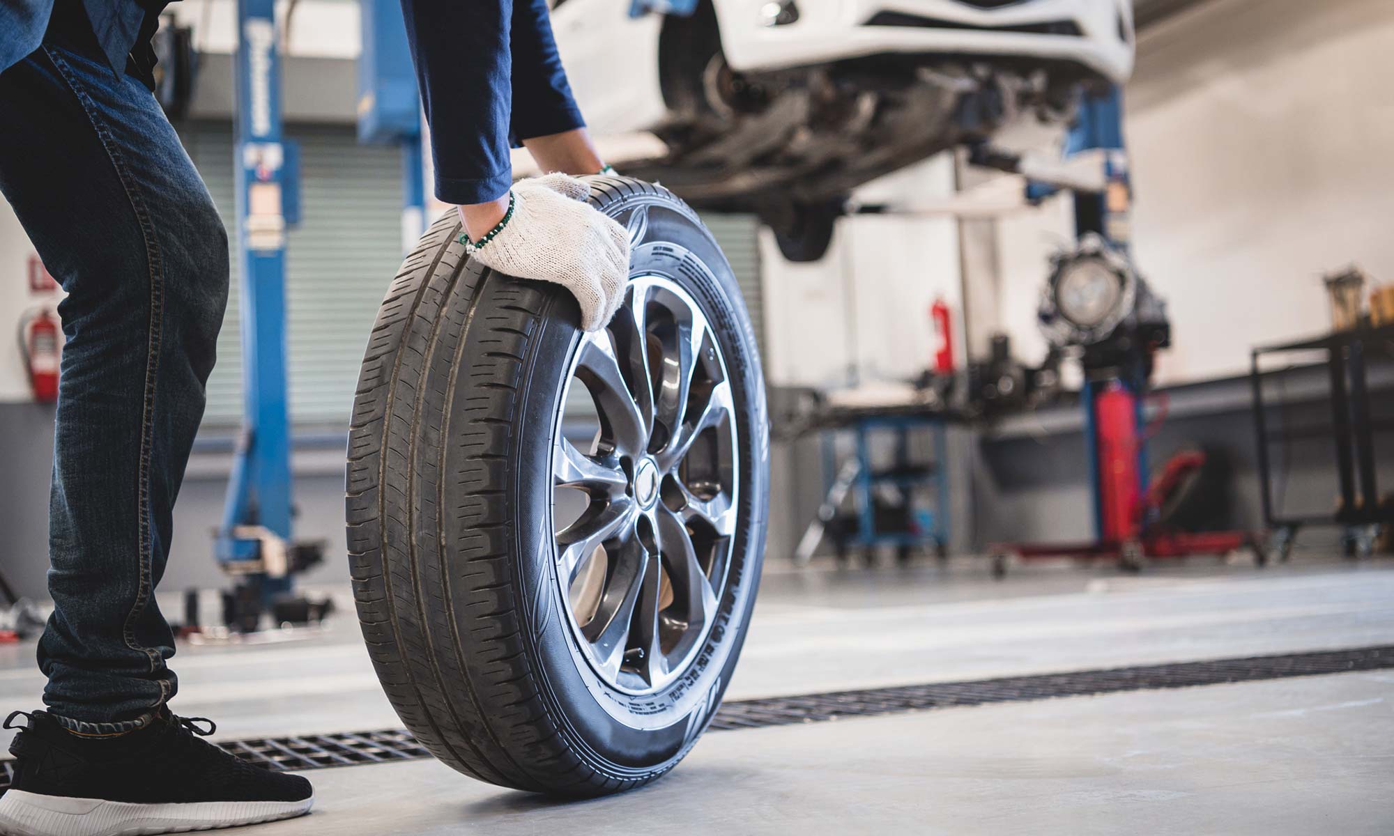 A car mechanic rolling a new tire across the shop floor.