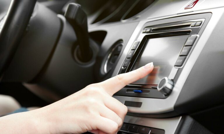 A close up of a person's hand touching their car's infotainment touch-screen display.