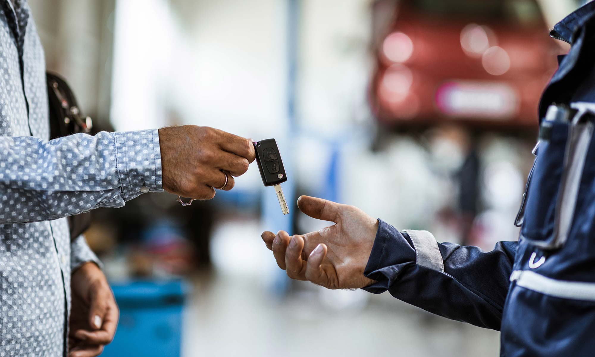 A closeup of a car mechanic handing back the keys of a vehicle to the customer.