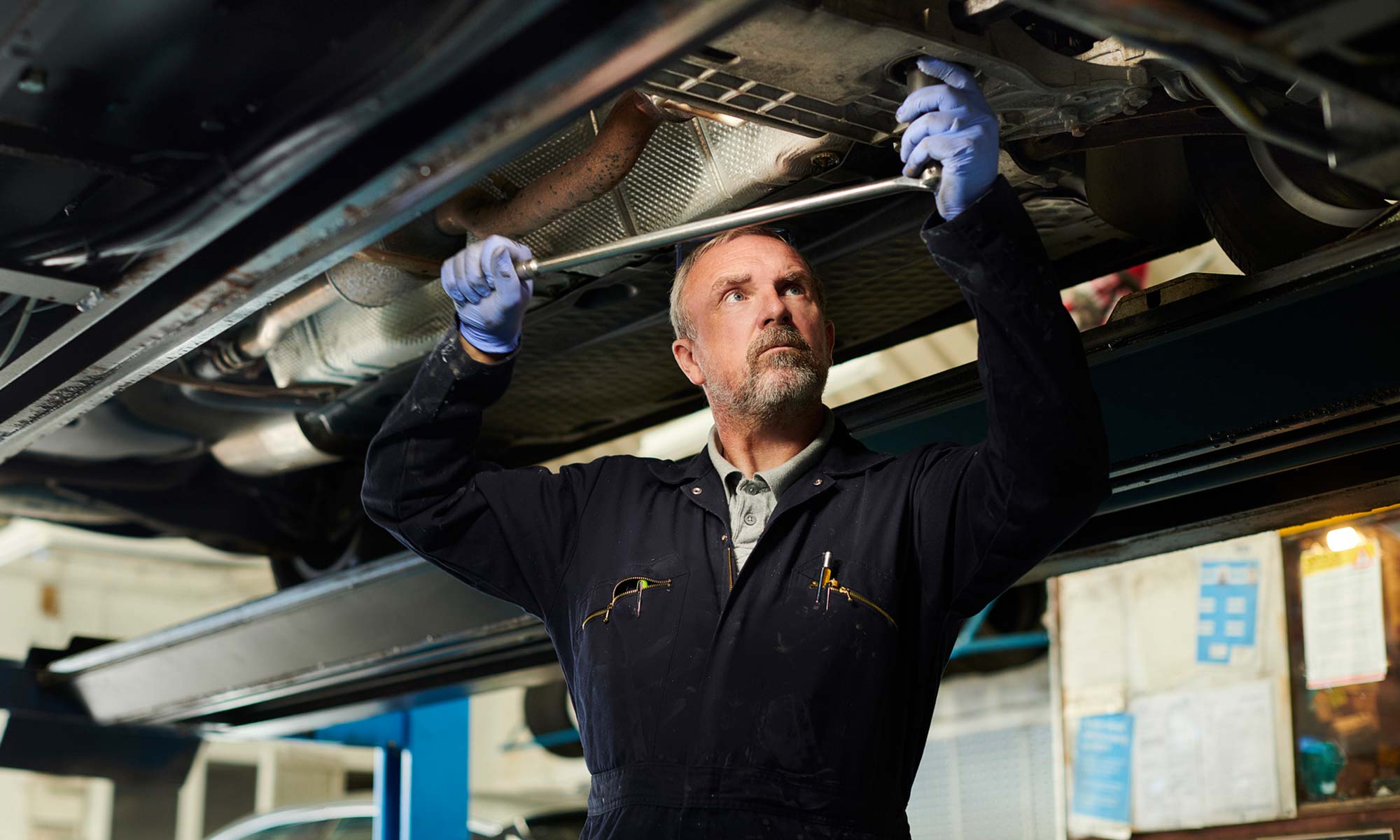 A car mechanic checking the undercarriage of a vehicle.