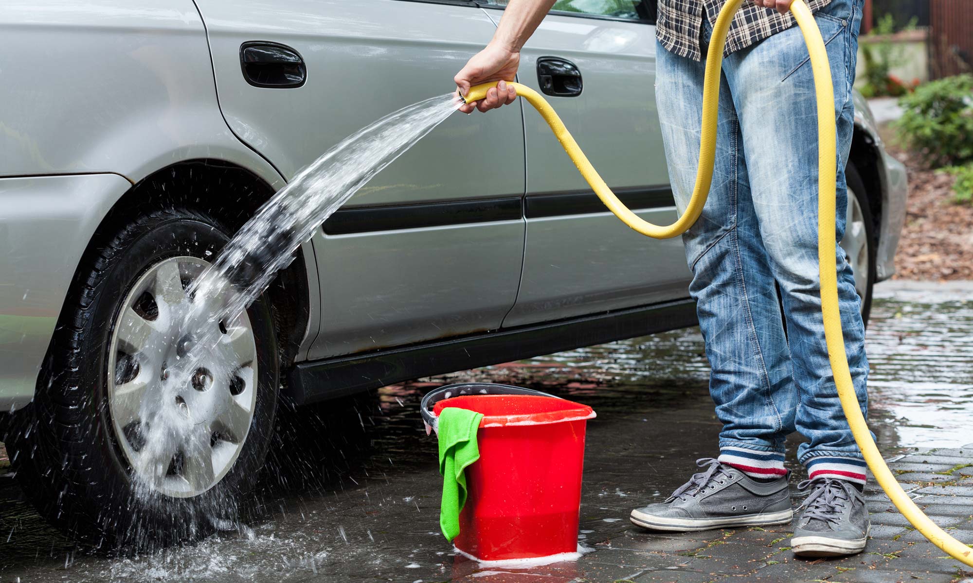 A may using a hose to clean his car's tire.