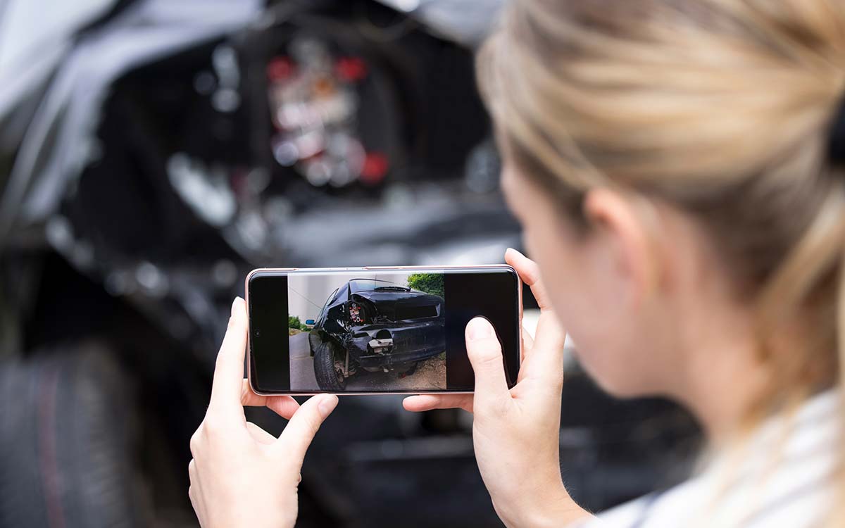 A woman taking a picture of her car after an accident. 