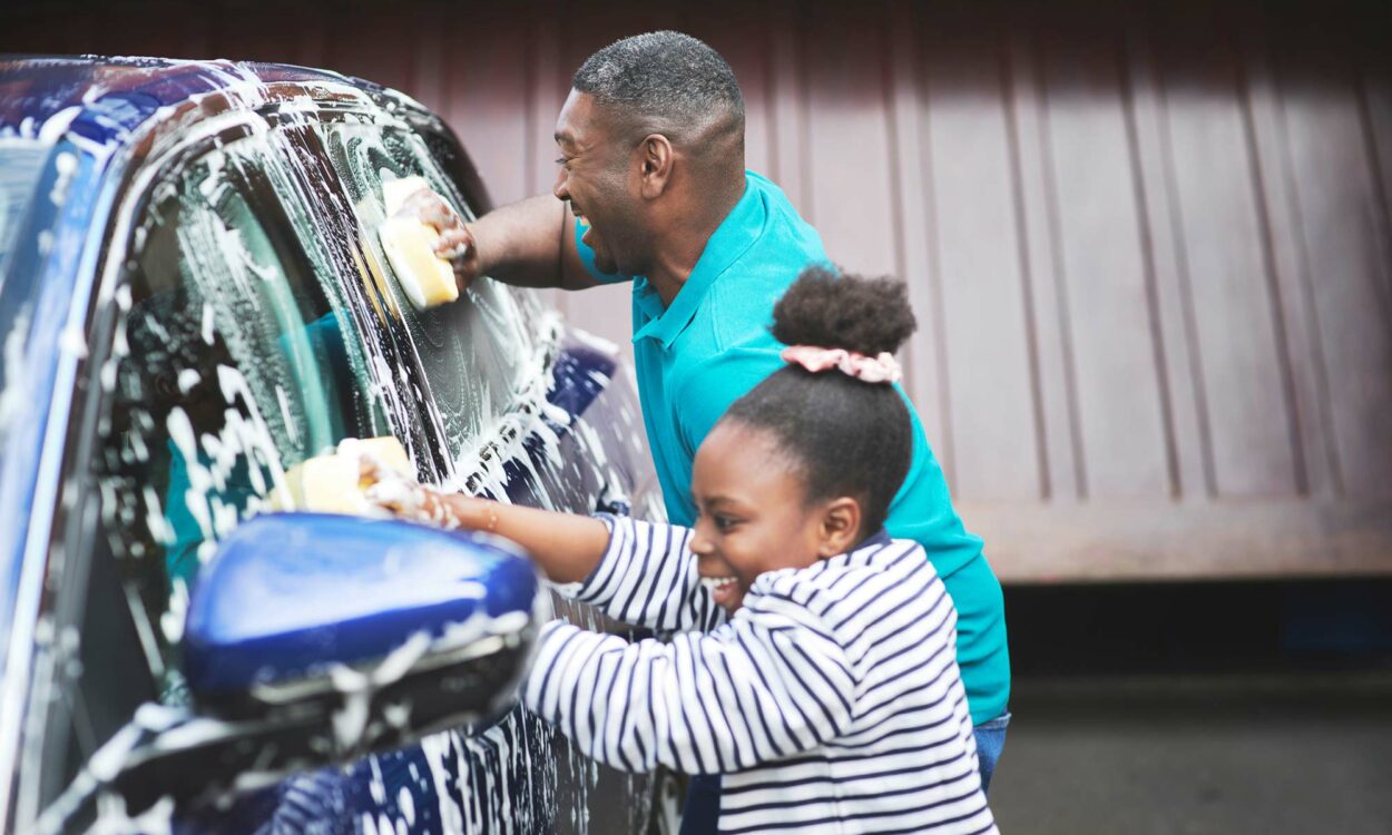 A father and his young daughter laugh while washing their car.