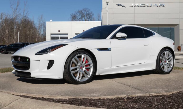 A whit Jaguar F-Type outside a dealership.