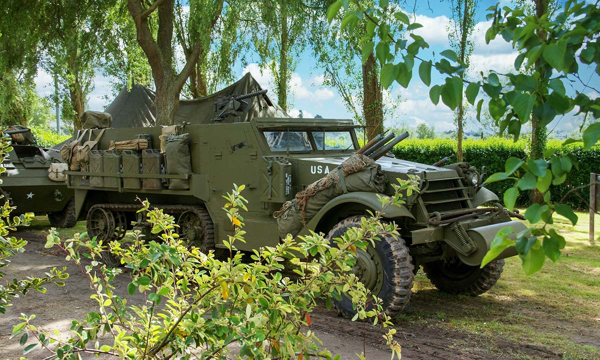 A M3 Half-Track traveling down a dirt road.