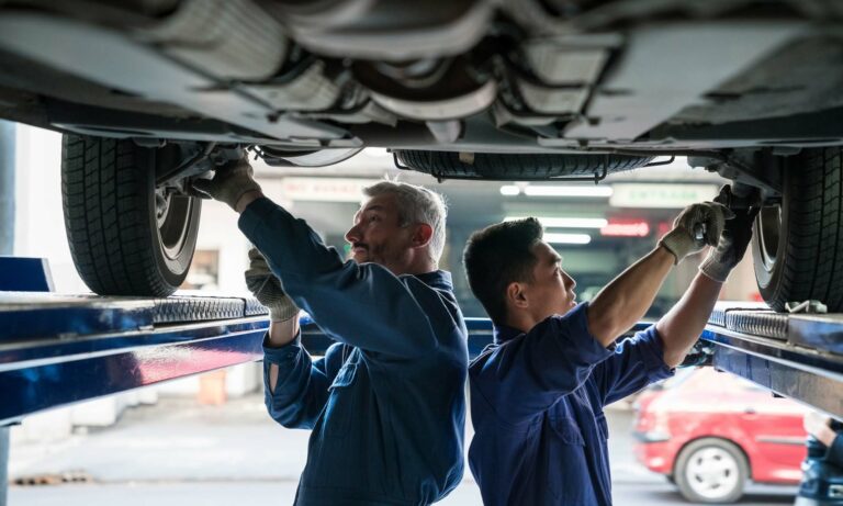 Two car mechanics checking a vehicle's brakes while it is on a lift.