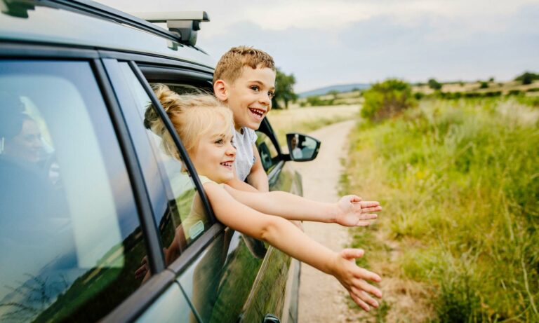 Two children laughing and sticking their heads out a car window.