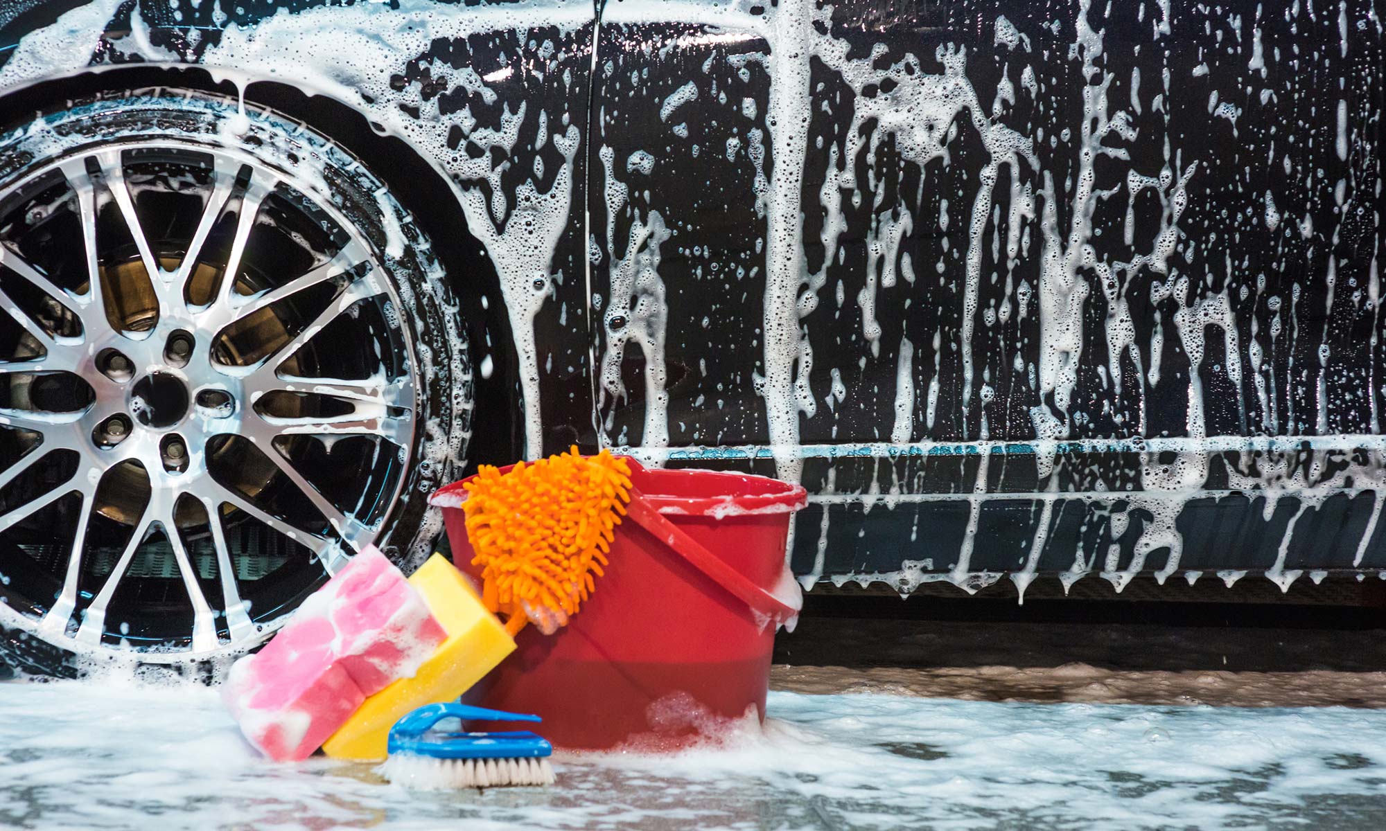 A bucket and cleaning supplies next to a soapy car.