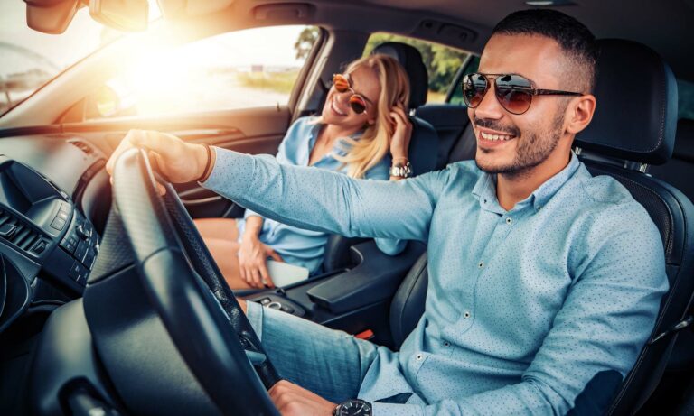 A young man and woman taking a summertime drive while wearing sunglasses.