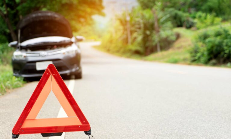 A warning triangle placed on the road in front of a vehicle with its hood popped open.