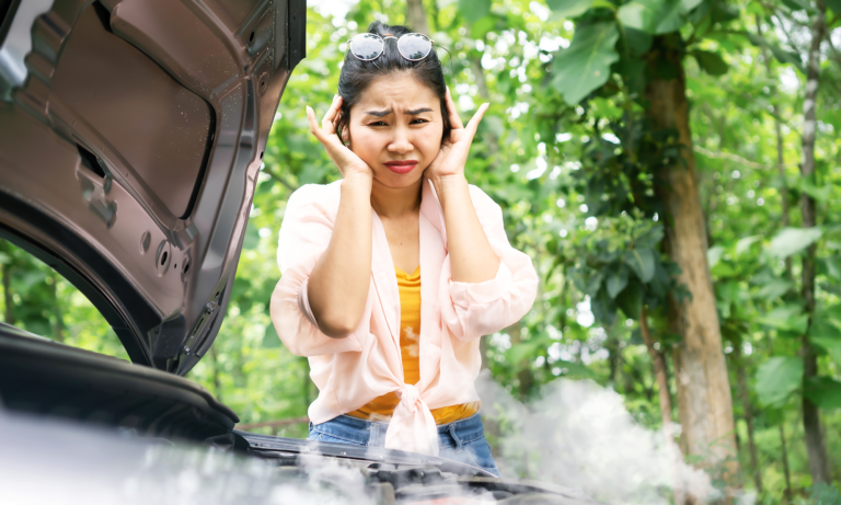 A young woman looking as steam comes out from her car's open hood.