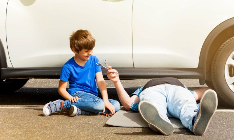 A young son helping his dad work on their car.