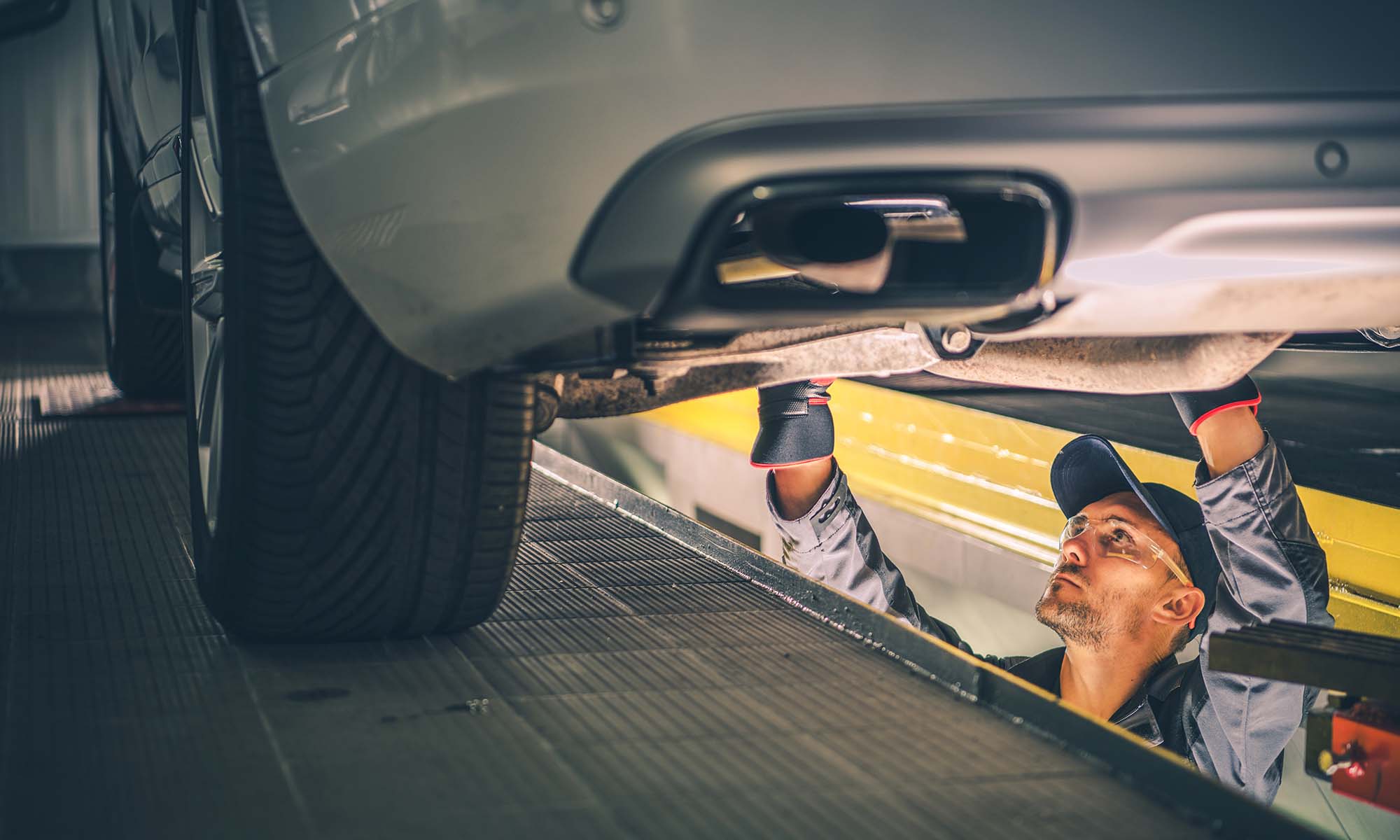 A mechanic checking the bottom of a vehicle that is propped up on a lift.