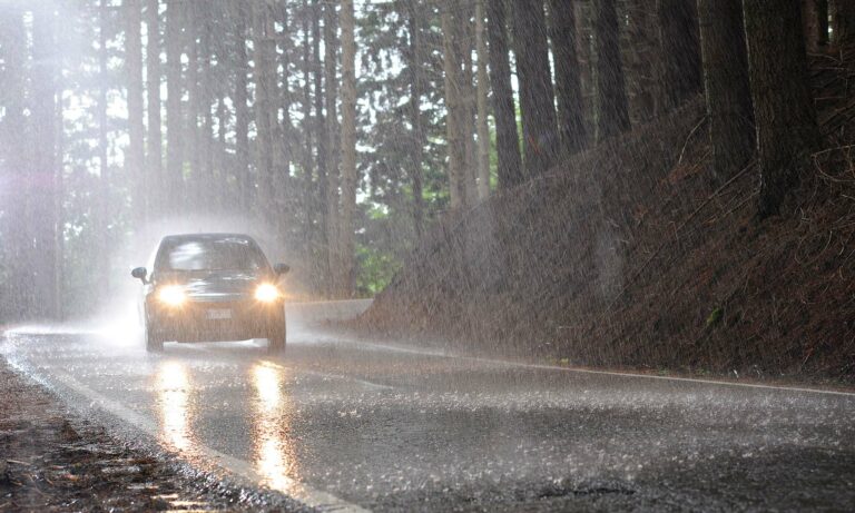 A car driving down a forest road during a rainstorm.