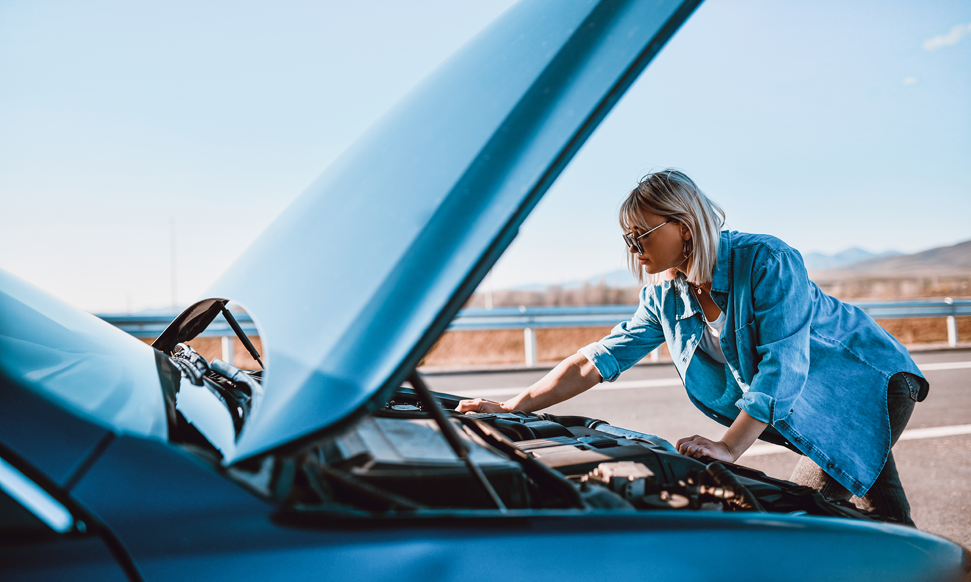 A young woman checking under the hood of her car after it stalls before calling her complimentary roadside assistance that comes with her Endurance Warranty auto protection plan.