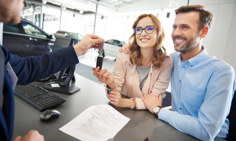 A couple at a car dealership receiving the keys to their brand new car.