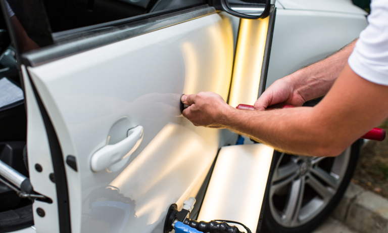 A man using a tool to remove a dent from a car's passenger side door.