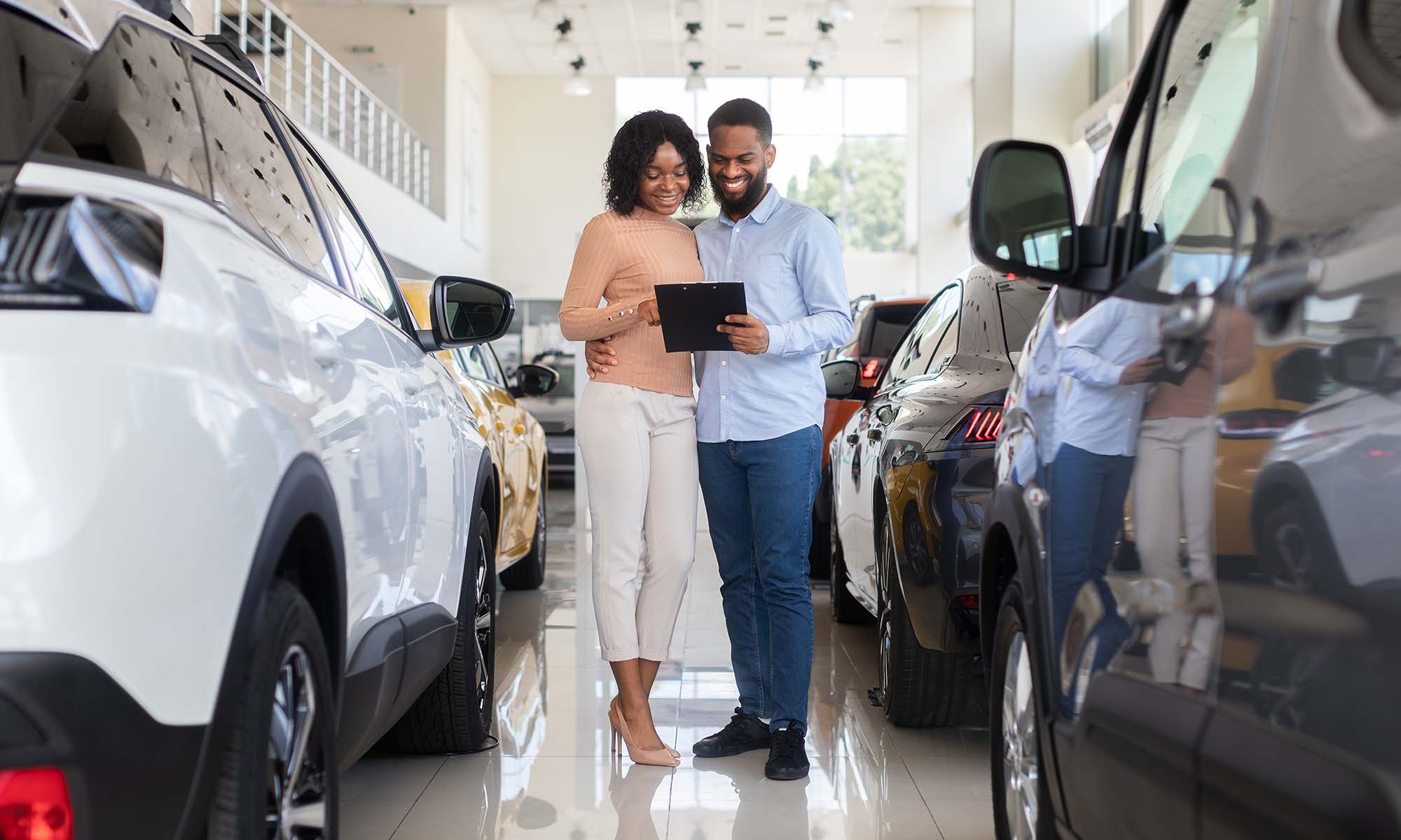 A young African American couple looking at brand new cars at a car dealership.
