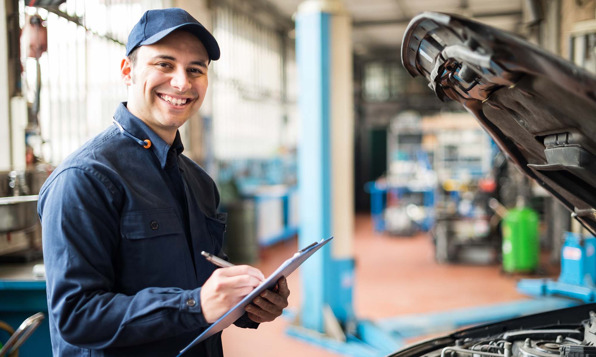 A car mechanic smiles while holding a checklist as he inspects under the hood of a vehicle. With an Endurance auto protection plan, you can take your car to any certified mechanic or repair shop of your choice.