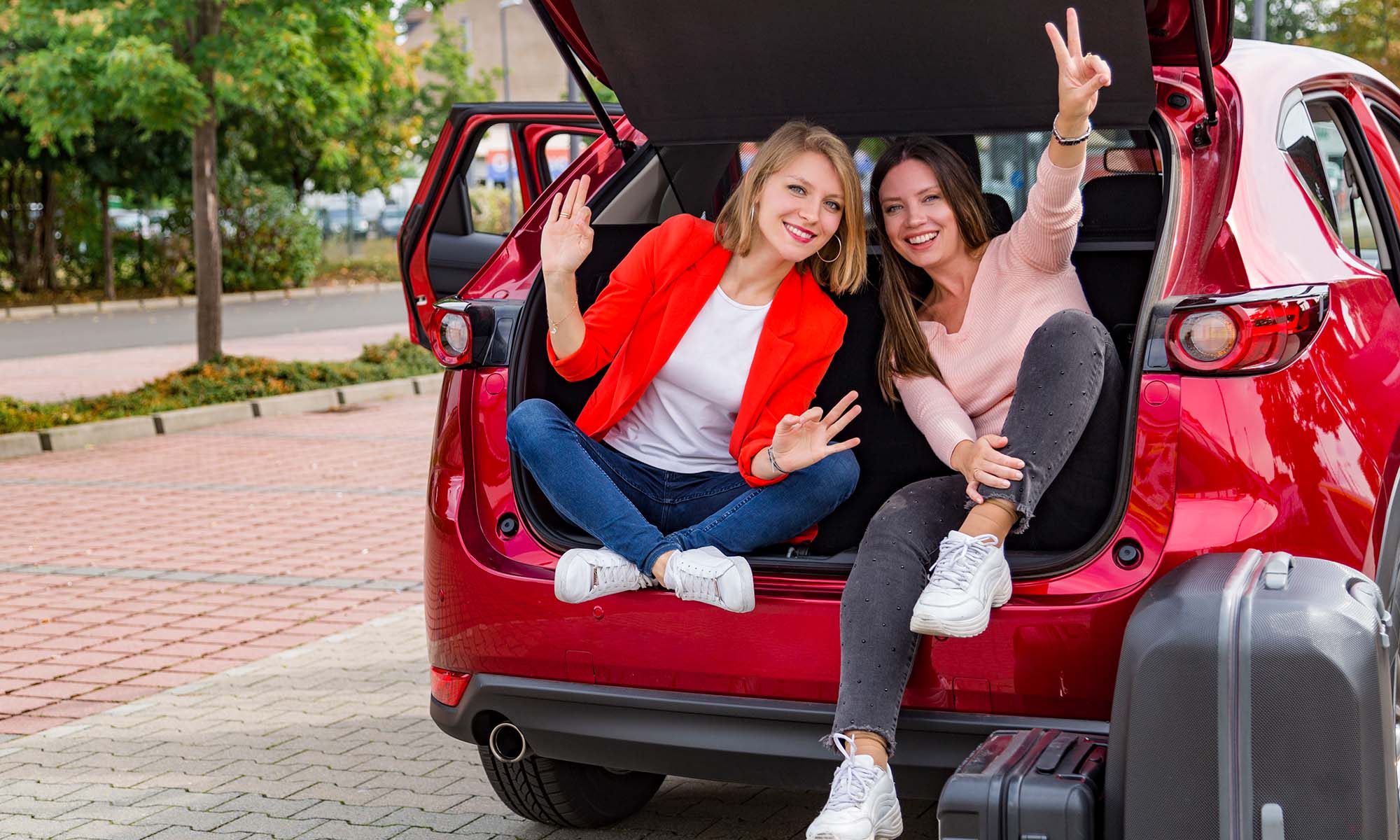 Two friends pose for a photo while sitting in the trunk of a car while moving into a college dormitory.