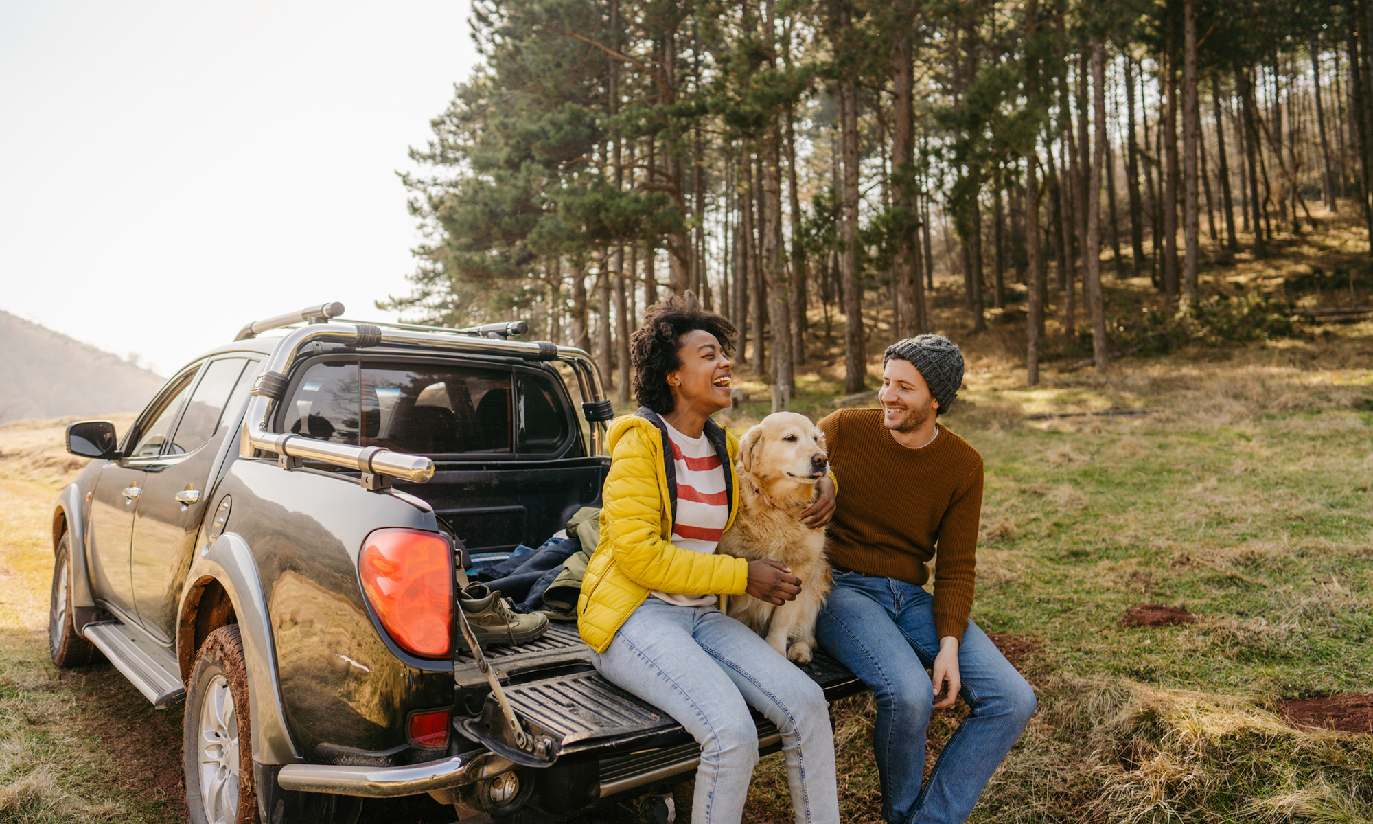 Una pareja y su perro se sientan y disfrutan del clima otoñal en la parte trasera de su camioneta.