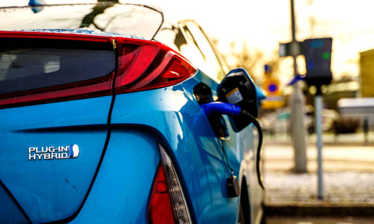 A blue plug-in hybrid vehicle charges at a charging station.