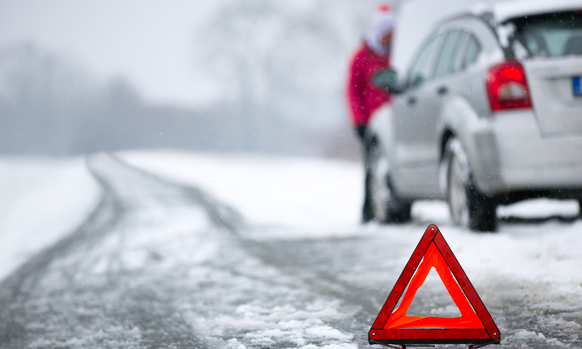 An emergency road triangle place in front of a pulled over vehicle on a snowy road.