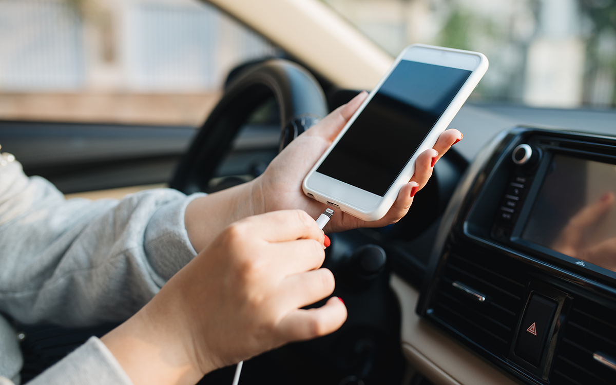 A close up of a young woman's hand plugging her phone into a car charger.