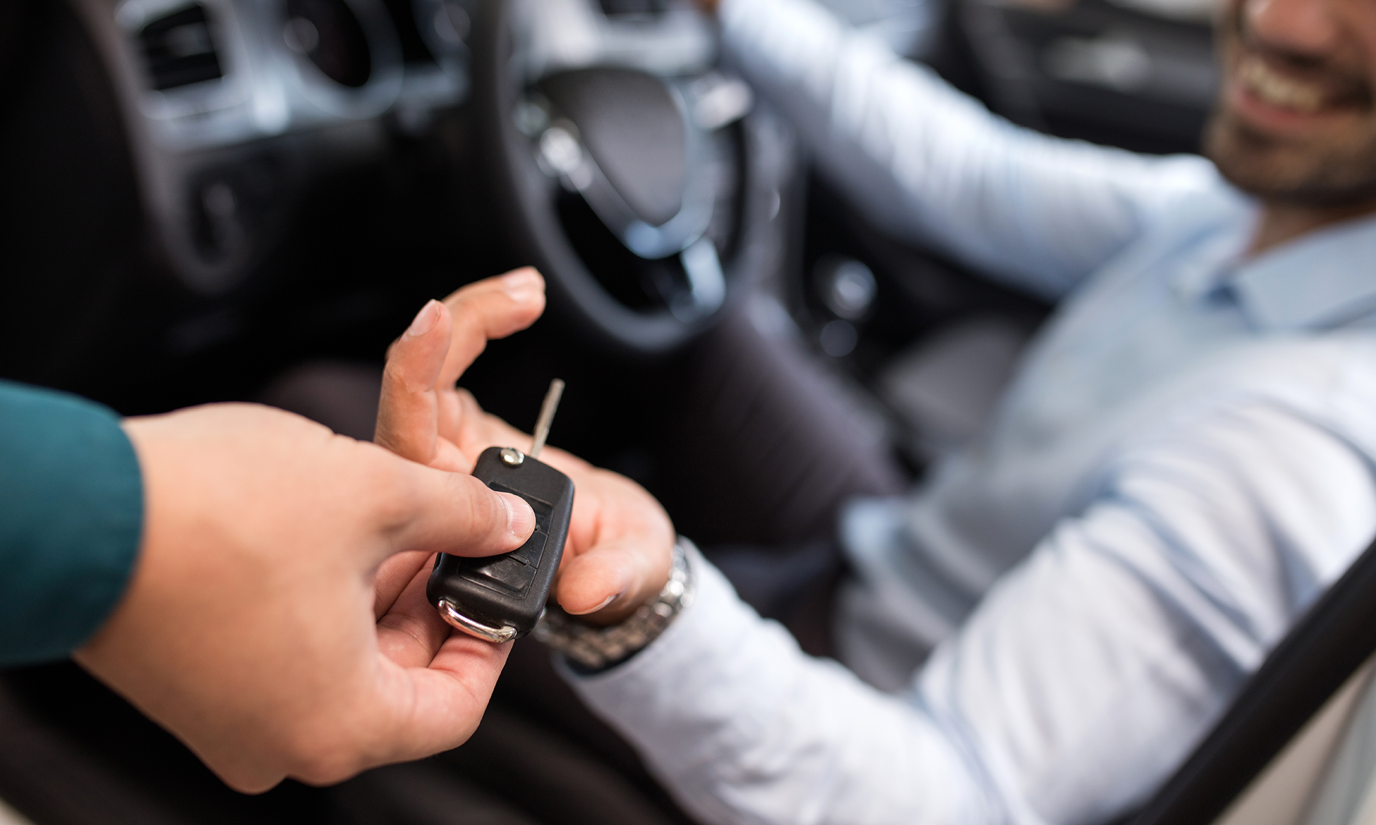 A young man being handed the keys to his rental car, which he reserved using a rental car subscription service.