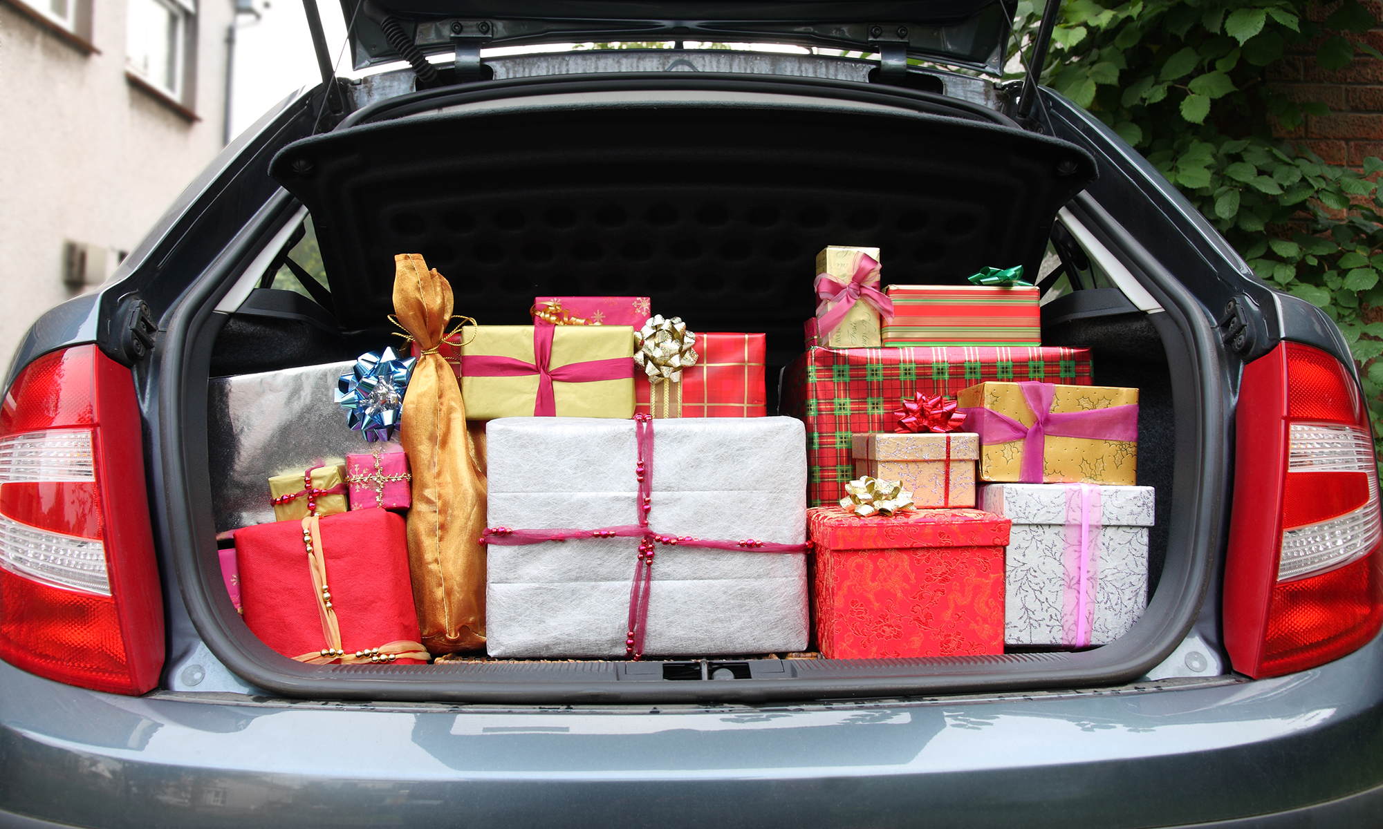 Holiday gifts of various sizes and wrappings sit in an open trunk of a car.