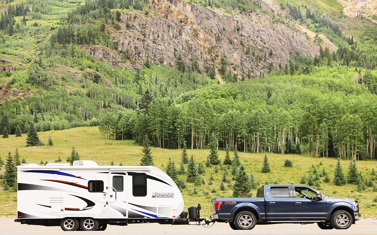 A 2015 Ford F-150 truck towing a camper trailer in front of a mountain background. 