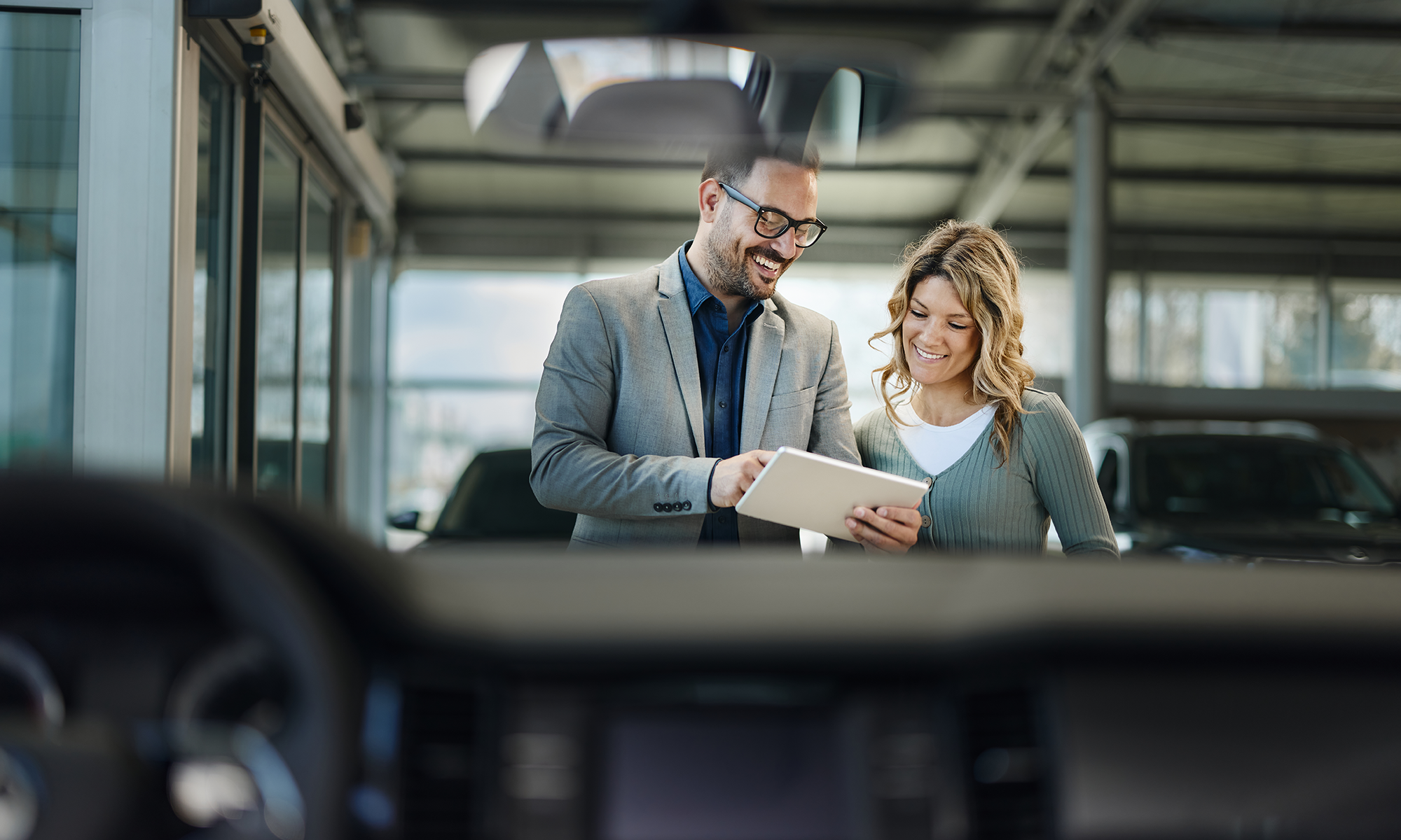 A car salesman speaks with a female customer in front of a vehicle.