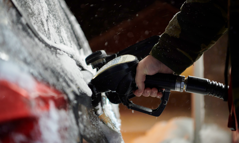 A close up image of a person filling up their car with gas with snow and ice on the vehicle.