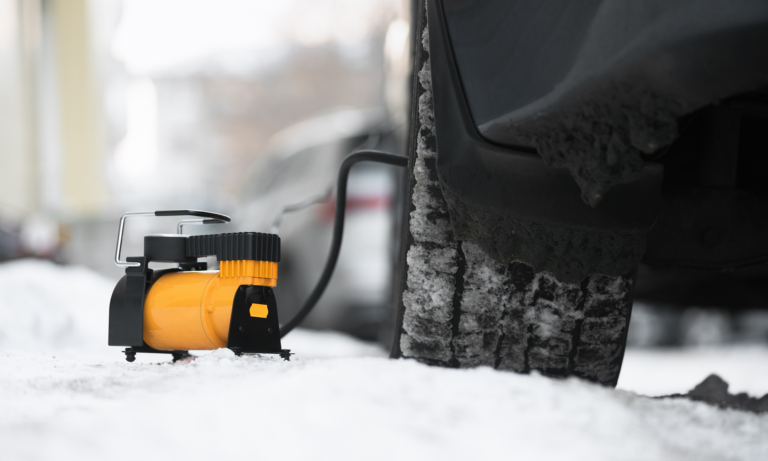 A portable air pump inflating a car's tire outside in the snow.