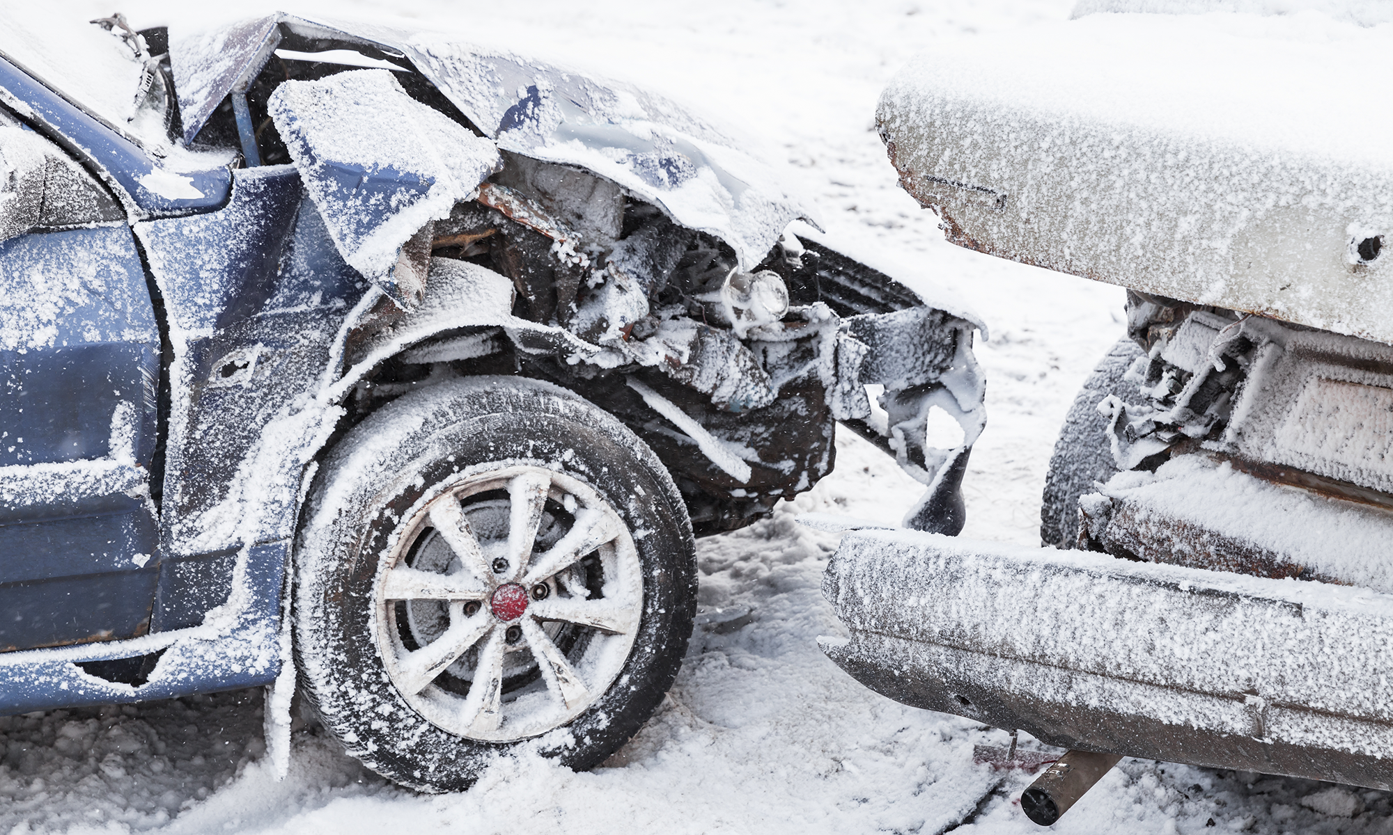 A close up image of 2 cars that have gotten into an accident on a snow covered road.