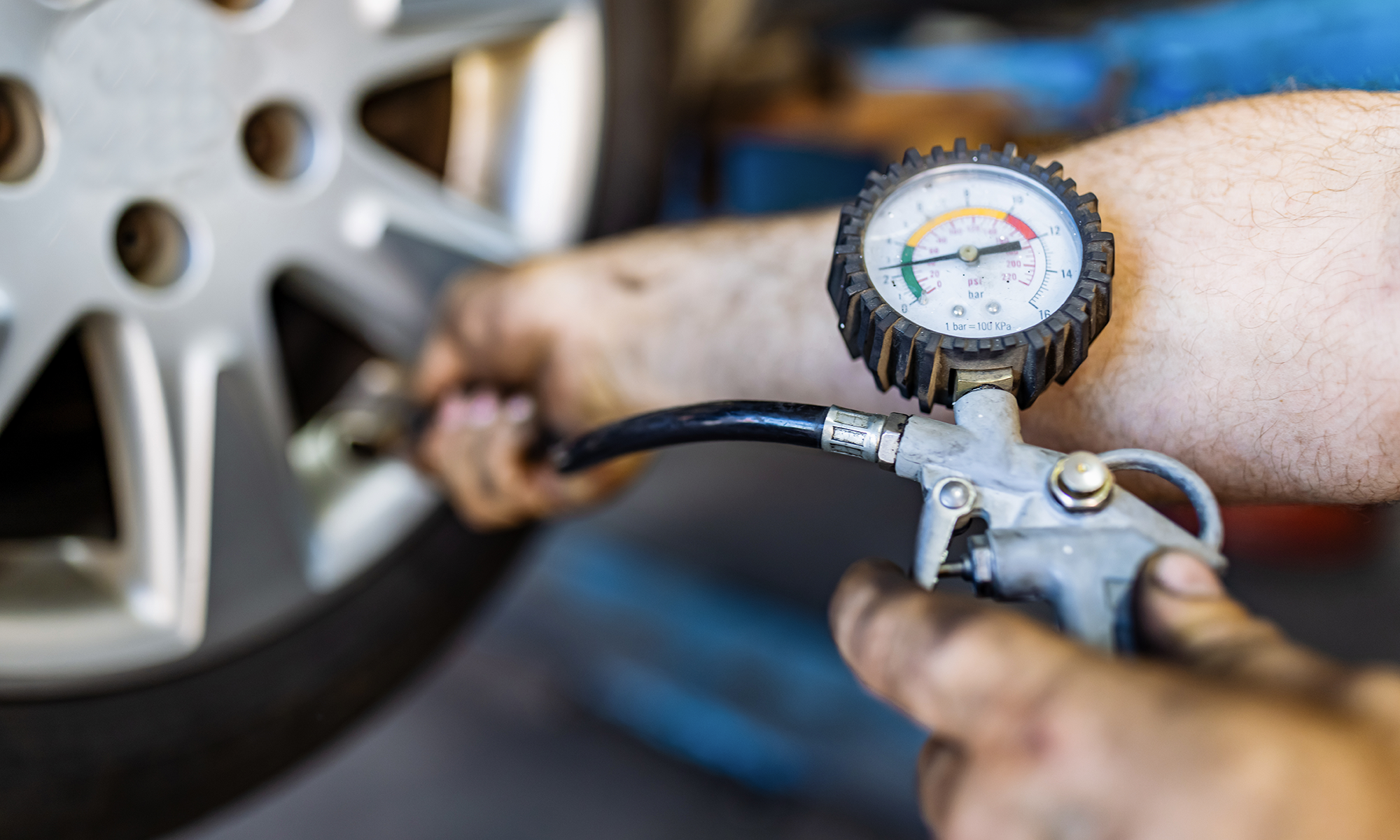 A closeup of a mechanic using a pressure gauge to measure a car's tire pressure.