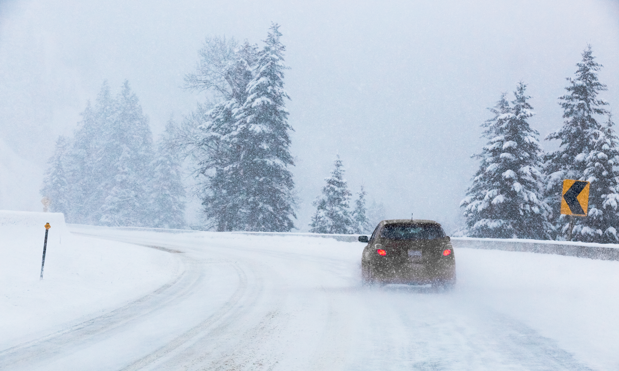 An orange sedan driving down a snowy rural highway.