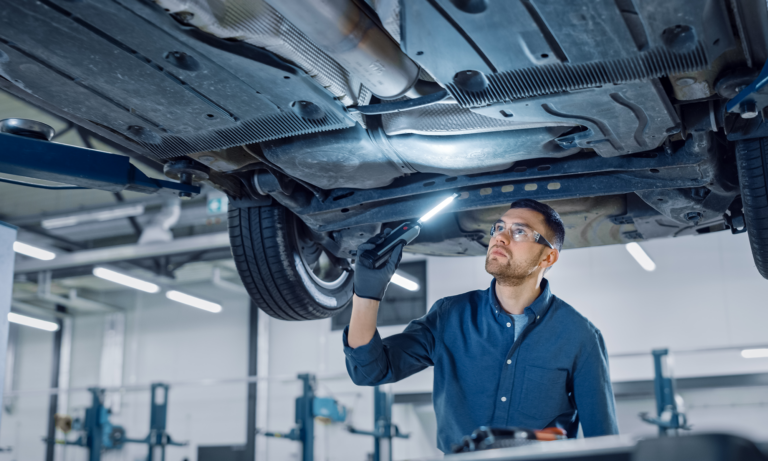 A car mechanic inspecting the undercarriage of a car on a lift.