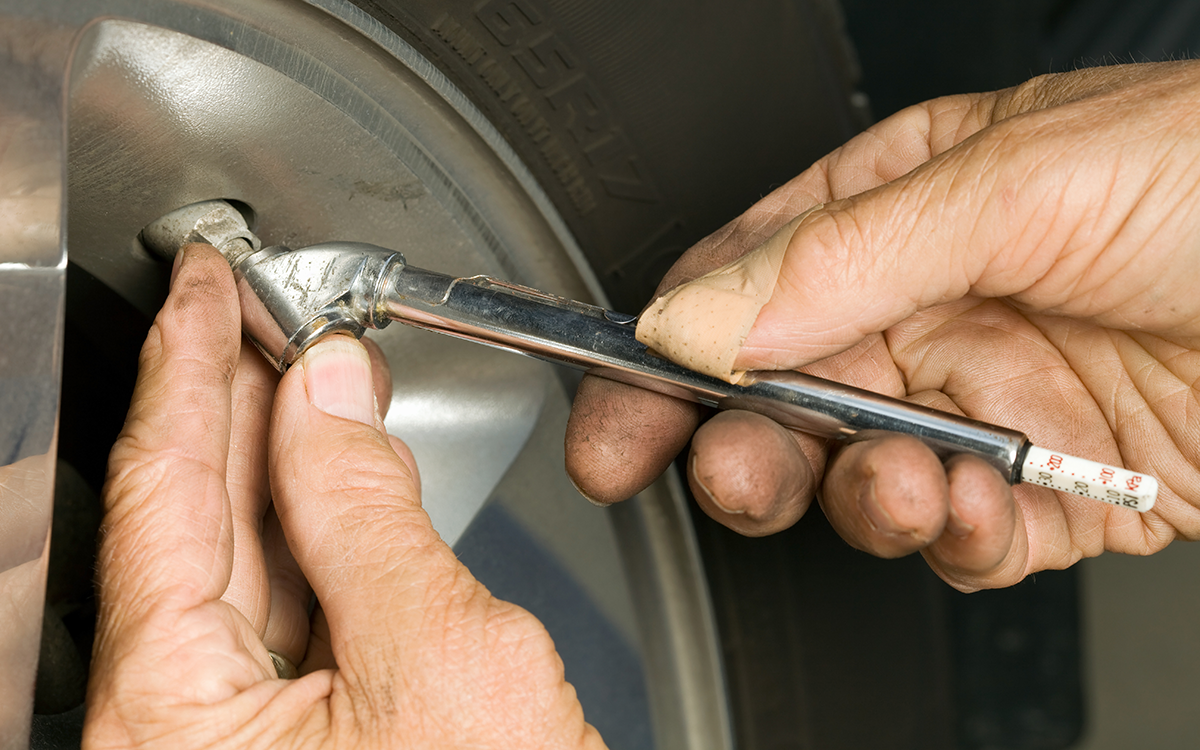 A close-up of a person's hand checking the tire pressure of a vehicle using a tire pressure guage.