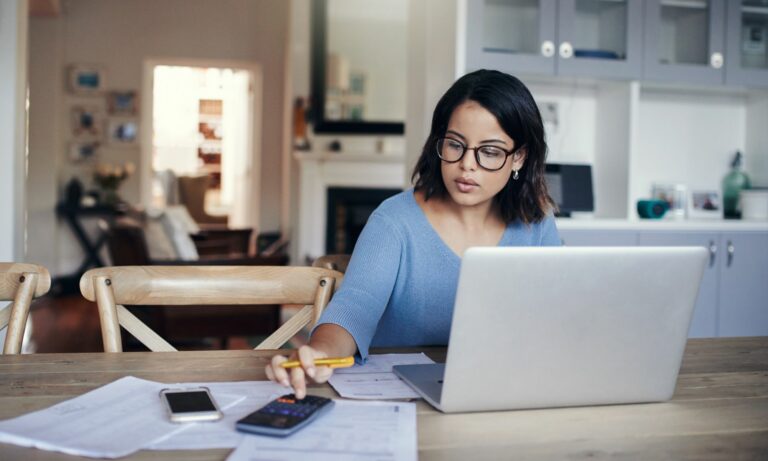 Woman using a laptop and calculator to work on her car payment