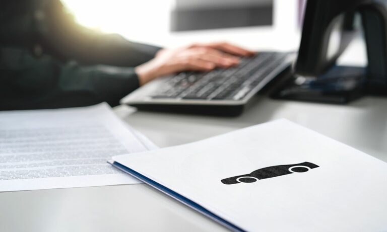 Car paperwork on a desk with a computer